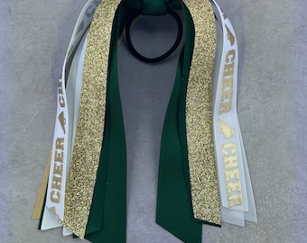 May include: Green, gold and white cheer bow with a black hair elastic. The bow has gold glitter ribbon and white ribbon with the text "CHEER" in gold.