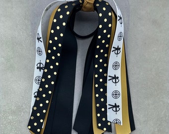 May include: Black and gold polka dot ribbon, black ribbon, and white and gold ribbon with a target and archer design hair tie.
