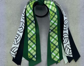 May include: Green, black and white ribbon hair tie with a volleyball pattern. The hair tie is tied in a bow with the ribbons hanging down.