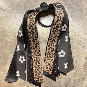 May include: Black and brown leopard print ribbon hair tie with black ribbon and white soccer ball print ribbon.