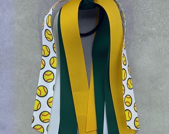 May include: A hair tie with green, yellow and white ribbons. The white ribbon has a pattern of yellow softball designs.