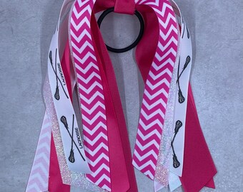 May include: Pink and white chevron patterned hair ties with a black lacrosse stick design and the word "Lacrosse" on the white ribbon.