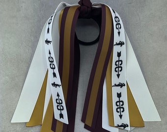May include: A hair tie with maroon, gold and white ribbons. The ribbons have a black running figure and arrow design. The hair tie is tied in a bow.