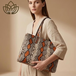 May include: A structured tote bag featuring a bold snakeskin pattern in shades of burnt orange, grey, and black. The bag has two top handles and a rectangular silhouette. A logo with a lotus flower icon and the text KHUSHI is visible.