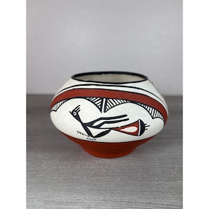 May include: A rounded ceramic bowl featuring a cream-colored base with a wide terracotta band around the center. The exterior is decorated with black line art depicting a stylized bird in flight, accented by geometric patterns and a solid terracotta base.
