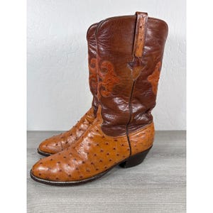 Könnte beinhalten: Ein Paar braune Cowboystiefel aus Leder mit einem strukturierten, genoppten Vorderblatt in einem helleren Beigeton und einem glatten, dunkelbraunen Schaft mit Ziernähten. Die Stiefel haben eine spitz zulaufende Kappe und einen Absatz.