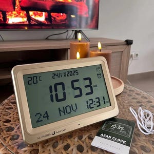 May include: A rectangular digital Azan clock with a gold-colored frame and a large LCD screen displaying the time 10:53 AM, the date 24/11/2025, temperature 20C, and prayer times. It includes a printed user guide and a white USB charging cable.