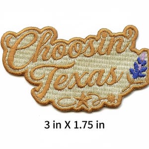 Peut inclure: Un écusson brodé avec le texte "Choosin' Texas" en écriture cursive marron sur un fond beige clair. L'écusson comprend une petite icône de fleur bleue et violette ainsi qu'une étoile. Il mesure 7,62 cm sur 4,45 cm au total.