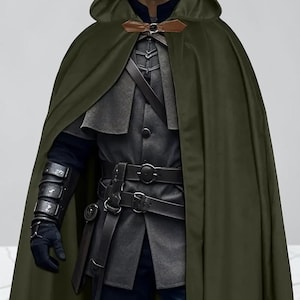 May include: A dark olive green hooded cloak with a brown leather-like clasp at the neck. The garment is worn over a dark gray jacket featuring a high collar, multiple black leather belts with silver-toned buckles, and black forearm bracers.