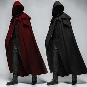 May include: Two floor-length hooded cloaks, one in deep red and one in black, each featuring a structured hood, a layered shoulder capelet, and intricate decorative trim along the front edges, worn over dark trousers and black leather boots.