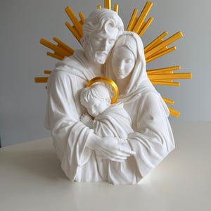 May include: A white sculpture of a family consisting of two adults and a child held in their arms. The figures have smooth, matte surfaces. Behind the adults is a bright yellow sunburst halo, and the child has a small yellow halo above their head.