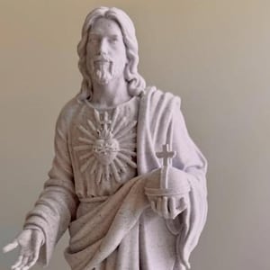 May include: A light gray speckled statue of a figure with long hair and a beard, wearing draped robes. The figure has a Sacred Heart emblem on the chest, holds a globus cruciger in one hand, and has the other hand extended forward.