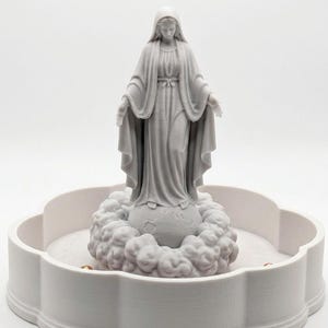 May include: A light gray 3D printed figurine of a standing figure with a draped head covering and long robes, arms outstretched, positioned atop a spherical base surrounded by sculpted clouds, all set within a circular scalloped tray.