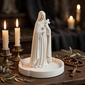 May include: A white figurine of a cloaked figure holding a small cross and a rose, standing on a circular white base. The figure wears a long, flowing robe with a hood covering the head, and the sculpture is crafted with smooth, matte details.