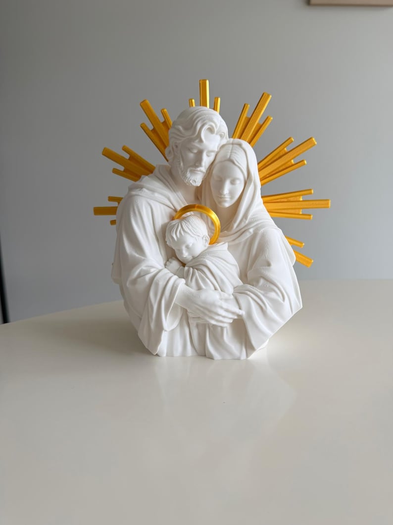 May include: A white sculpture of a family of three figures embracing, featuring a bearded adult, a woman, and a child. The child has a gold halo, and a large, radiating gold sunburst design is positioned behind the figures' heads.