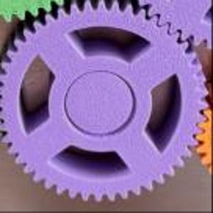 K&ouml;nnte beinhalten: Ein violettes Zahnrad mit einer zentralen kreisf&ouml;rmigen Nabe und vier symmetrischen Aussparungen zwischen den Speichen. Das Zahnrad hat eine texturierte Oberfl&auml;che und ausgepr&auml;gte Z&auml;hne am Au&szlig;enrand, neben einem gr&uuml;nen und orangen Zahnrad.
