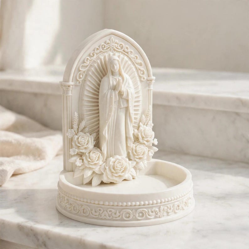 May include: A cream-colored resin trinket dish featuring a central relief of a figure with hands clasped in prayer, framed by an arched structure with floral rose accents and a decorative base with a beaded and scrollwork border design.