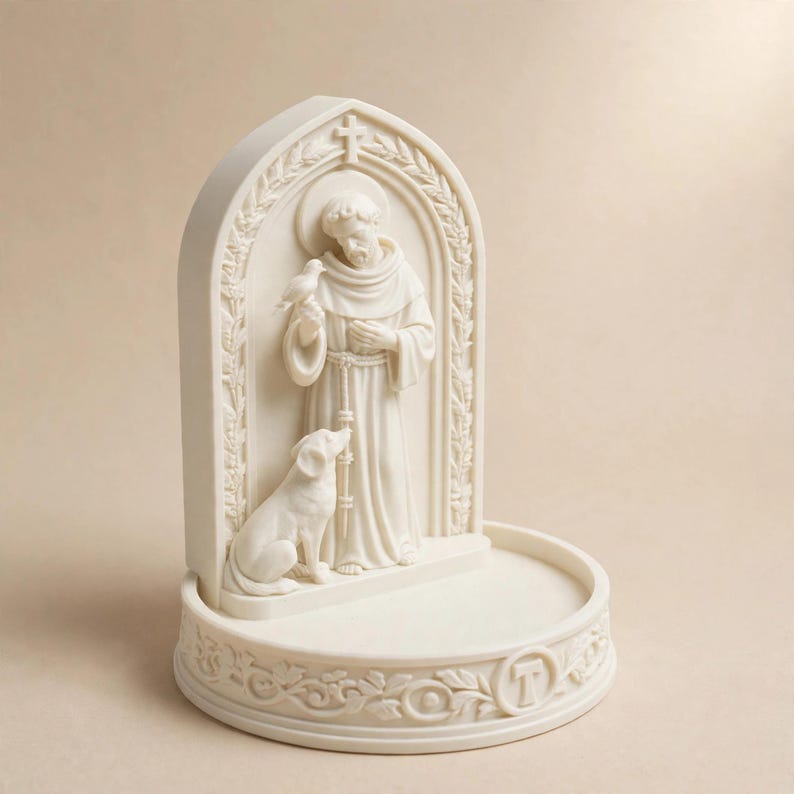 May include: An off-white, cream-colored resin sculpture featuring a figure in robes standing within an arched frame. The figure holds a small bird, with a dog sitting at their feet. The base is circular and decorated with floral carvings and a letter T.