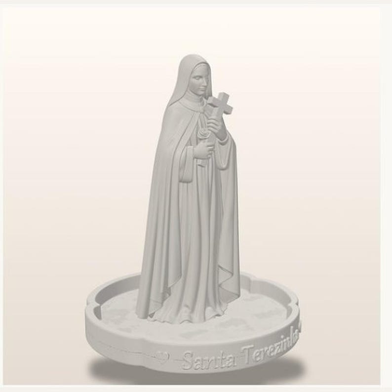 May include: A light gray monochromatic figurine of a nun wearing a habit and veil, holding a cross and a rose. The figure stands on a circular base with a scalloped edge, featuring the embossed text Sarita Terezinha along the front side.