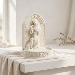 May include: An off-white, arched sculpture featuring a robed figure standing with a bird perched on one hand and a dog sitting at their feet. The base is circular with a decorative border and a central letter T, all rendered in a matte finish.