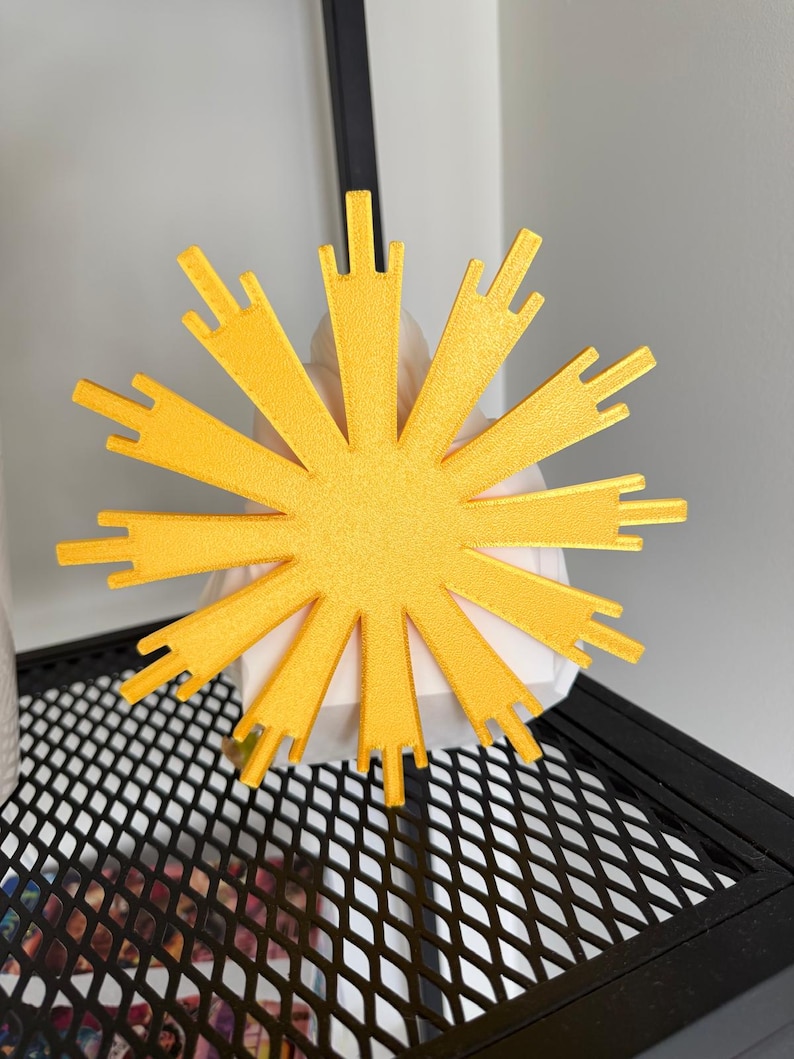 May include: A bright yellow, star-shaped decorative object with multiple radiating points of varying lengths. The object features a textured surface and is positioned in front of a white, geometric, faceted base, creating a high-contrast visual display.