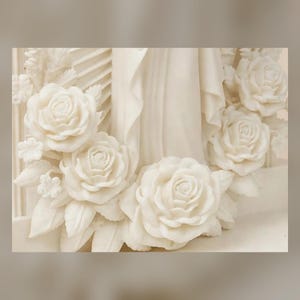 May include: A cream-colored sculpture featuring a central figure draped in flowing fabric, surrounded by a detailed arrangement of sculpted roses and leaves. The entire piece is monochromatic, showcasing intricate floral textures and smooth folds.