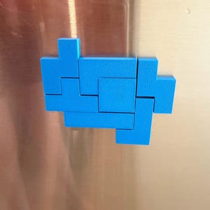 Op de afbeelding: Een set felblauwe geometrische kunststof blokken gerangschikt in een cluster. De stukken hebben een getextureerd oppervlak en zijn gevormd als verschillende in elkaar grijpende puzzelcomponenten, die lijken op klassieke videospelblokvormen.
