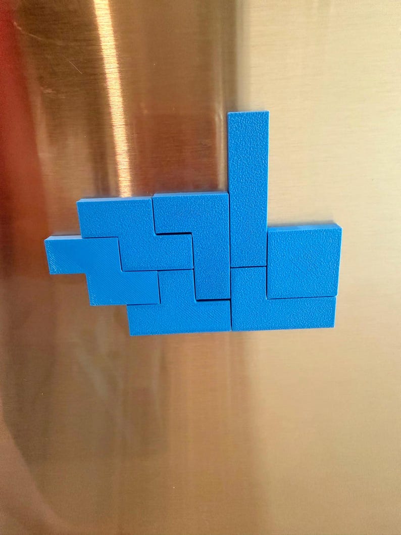 Op de afbeelding: Een set felblauwe geometrische kunststof blokken gerangschikt in een cluster op een metalen oppervlak. De stukken hebben de vorm van verschillende Tetris-achtige polyomino's, met een getextureerde matte afwerking en scherpe, strakke randen.