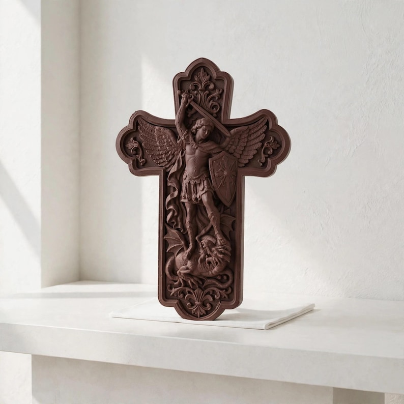 May include: A dark brown, intricately carved wooden cross featuring a relief sculpture of Saint Michael the Archangel with wings, holding a sword and shield while standing over a dragon, framed by ornate floral and scrollwork detailing.