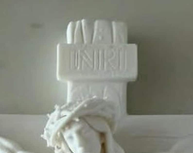 May include: A white matte sculpture of a crucifix featuring a figure wearing a crown of thorns. The top section of the cross displays the embossed text INRI. The entire object is rendered in a solid, uniform white finish with detailed carvings.