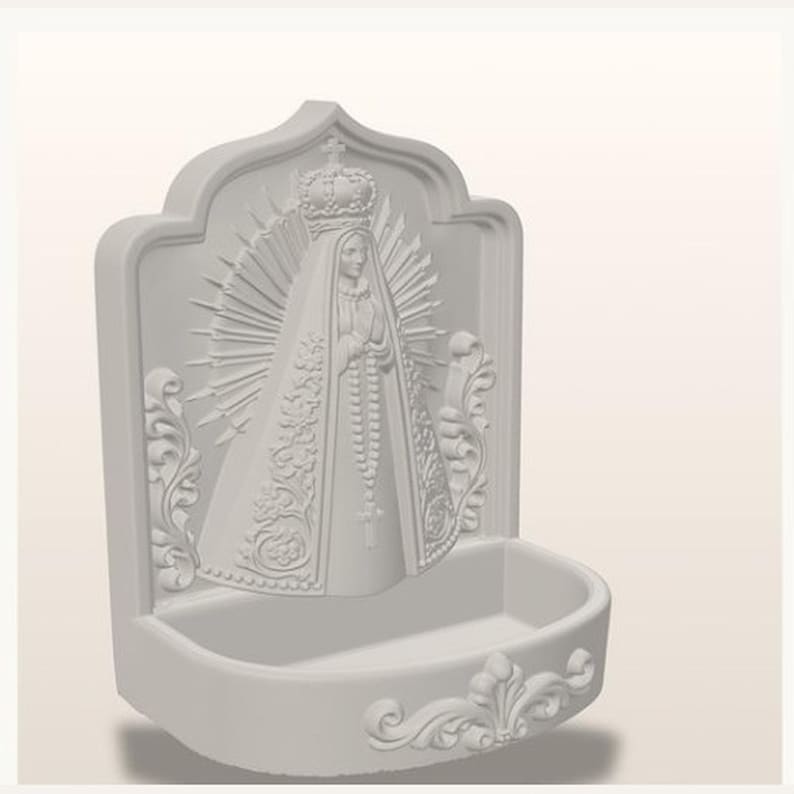 Puede incluir: Una pila de agua bendita blanca para pared con una escultura en relieve de una figura coronada con halo, que viste una t&uacute;nica larga con patrones florales intrincados y sostiene un rosario. La base es un cuenco semicircular con volutas.