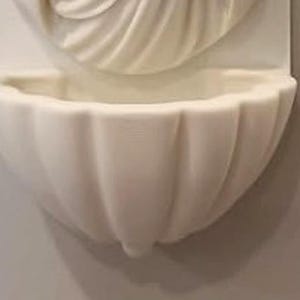 May include: A wall-mounted off-white basin featuring a scalloped shell design. The basin is attached to a rectangular backplate that displays a carved, fan-like pattern extending upwards from the centre of the bowl, creating a cohesive unit.