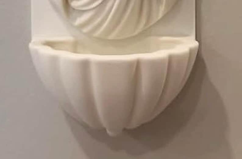 May include: A wall-mounted off-white basin featuring a scalloped shell design. The basin is attached to a rectangular backplate that displays a carved, fan-like pattern extending upwards from the centre of the bowl, creating a cohesive unit.