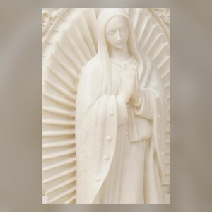 May include: A cream-colored off-white sculpture of a figure with a hooded head and hands pressed together in a prayer position. The figure is centered against a large, circular, radiating sunburst halo design with textured, linear rays.