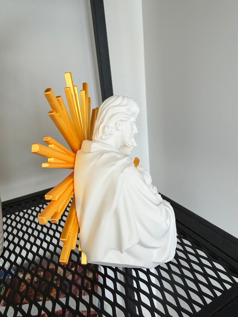 May include: A white bust of a bearded figure draped in a robe, viewed from the side. Behind the figure is a bright gold sunburst halo consisting of multiple radiating rectangular beams of varying lengths, extending outward from the center.