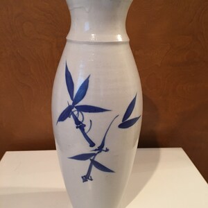 May include: A white ceramic vase with a blue and white bamboo design. The vase is tall and slender with a rounded bottom and a narrow neck.