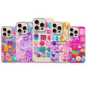 Puede incluir: Cinco fundas para smartphone con gráficos coloridos y translúcidos de diversas formas, incluyendo cubos, esferas y alimentos. Los diseños incluyen el texto "NEE DOH" y "She LOVES NEEDOHS" en varias tipografías sobre fondos vibrantes de color rosa, azul y transparente.