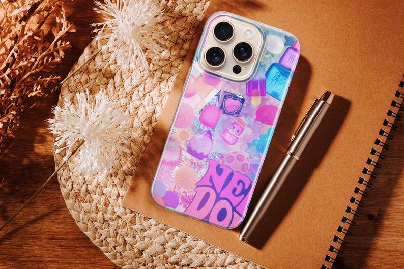 May include: A clear smartphone case featuring a vibrant collage of colorful candy, ice cream, and dessert illustrations, including the text "NE DO" in bold purple letters, designed for a device with a triple-lens camera system on the back.