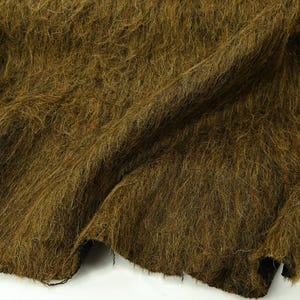 May include: A piece of fabric with a long, shaggy, and textured pile in a deep olive brown colour. The material features a dense, fibrous surface with visible strands that create a wild, unkempt appearance across the entire folded textile surface.