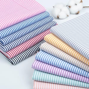 May include: A collection of folded fabric squares featuring various thin vertical stripe patterns in colours including pink, blue, red, black, grey, yellow, tan, purple, teal, and peach, accompanied by two white cotton bolls.
