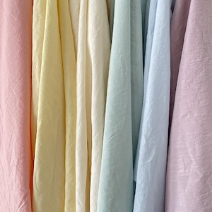 May include: A collection of vertically draped fabric swatches in a soft pastel colour palette. The textile selection includes shades of light pink, pale yellow, cream, mint green, sky blue, and lavender, all featuring a subtle, textured weave.