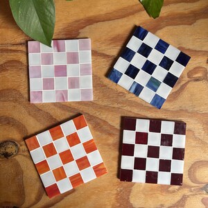 May include: Four square coasters arranged in a grid, each featuring a checkerboard pattern of white tiles alternating with colored tiles in shades of light pink, deep blue, bright orange, and dark maroon, all crafted from smooth glass pieces.