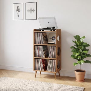 May include: A light brown wooden record storage cabinet with three shelves filled with vinyl records, standing on four tapered legs. A black turntable with a clear dust cover sits on the top surface. The side panels feature circular cutouts.