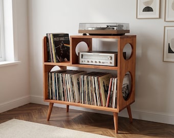 May include: A wooden record player stand with tapered legs, featuring a top shelf for a turntable and receiver, and a lower shelf for vinyl records. The unit has circular cutouts on the side panels and holds a collection of records including a Miles Davis album.