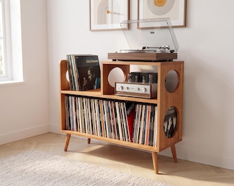 May include: A wooden record player console with tapered legs, featuring a top surface for a turntable and amplifier, and two lower shelves filled with vinyl records. The unit has circular cutouts on the side panels and a warm brown wood finish.