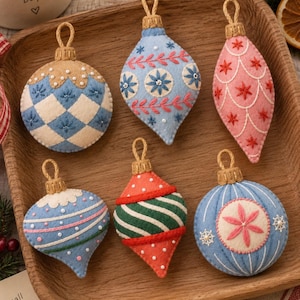 May include: Six felt Christmas ornaments with intricate embroidery and hanging loops. The collection includes round and teardrop shapes in blue, white, pink, green, and red, featuring patterns like diamonds, stripes, and floral star motifs.