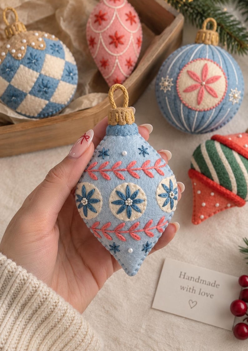 May include: A collection of teardrop and round felt Christmas ornaments featuring intricate embroidery in blue, pink, green, and cream. Each ornament is decorated with stitched floral patterns, small white beads, and a gold-colored hanging loop.