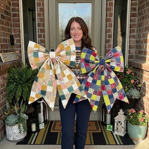 May include: Two large decorative bows made from quilted fabric patches. The left bow features a patchwork of soft yellow, cream, sage green, and floral patterns. The right bow displays a vibrant patchwork of navy blue, bright lime green, and red floral prints.
