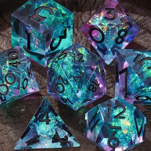 May include: A set of seven polyhedral dice made of translucent resin with an iridescent, shimmering blue and purple internal foil effect. Each die features sharp edges and bold, black engraved numbers for clear visibility during gameplay.
