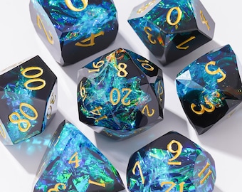 May include: A set of seven polyhedral dice featuring a dark resin base with embedded iridescent blue and green foil flakes. Each die has sharp edges and gold-colored engraved numbers. The set includes a d20, d12, d10, d8, d6, d4, and a percentile die.